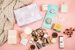 A closed My Thera Box subscription box surrounded by encouraging note cards, lip balm, skin care and other self care items.