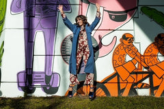 a model jumping up for joy about our clothing subscription box wearing a blue trench, patterned jumpsuit and velvet heels