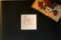 A close up of the black box with the Black Rose Horror Book Box logo, and a statue with a skull, red roses, and a raven on top of a book