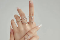 This photo shows a hand model modeling several initial style diamond encrusted gold rings on each finger showing what’s being sold