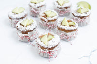 Mini golden apple cakes studded with apple bits, dusted with sugar, alongside muffin pan and baking tools