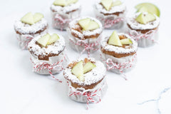Mini golden apple cakes studded with apple bits, dusted with sugar, alongside muffin pan and baking tools