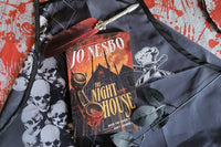 Black and white skull apron on top of a red and white scary paper, a red feather ink pen, and a book by Jo Nesbo called The Night House