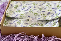 A purple box covered with lavender tissue paper and thank you sticker, with a crinkled paper around.