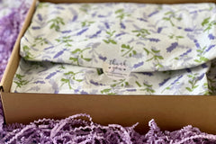 A purple box covered with lavender tissue paper and thank you sticker, with a crinkled paper around.