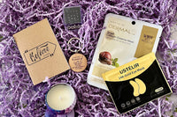 Close up look to Purple Box self-care items, such as scented candle, keychain, notepad, fidget toy, eye mask and face mask.