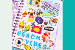 An open notebook with a Four Bears, summer themed sticker collage and letters shaped like waves spelling out beach vibes.