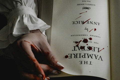 horror vampire book that has drops of dark red blood on it and a vampire looking hand holding the book.