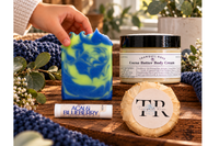 Hand holding handmade soap bar with blue and green swirls beside matching soap packaging            