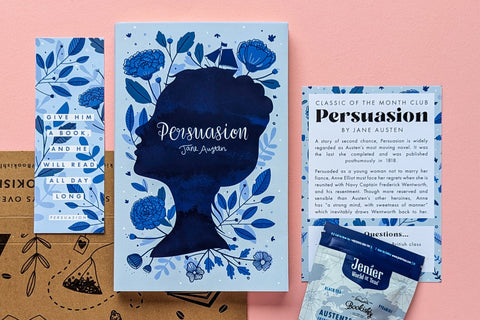 A hand holds three colorful Jane Austen book covers in a cozy setting, part of the TEA & BOOK CLUB subscription box for book lovers