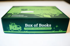 A Box of Books subscription box against a white background. Box has a truck with books and brand with slogan.