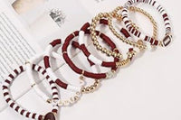 Loose Game Day stackable friendship bracelets in maroon and white beads with gold accents arranged diagonally on an open magazine page, show