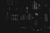 Dark or almost black and white photo of old bookshelf from a castle with books and other weird items like perpetual watches.