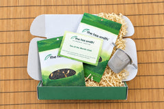 The Tea Smith tea of the month box open with two bags of tea spilling out with information card and tea infuser basket.