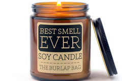 Lit Best Smell Ever 9oz soy candle by The Burlap Bag in an amber glass jar, black metal lid resting beside it on white