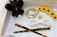 another example of an open box from the hair candy club, featuring a large sunflower clip, brown butterfly, soft hair ties and chopsticks