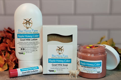 Goat milk lotion, soap, sugar scrub, and lip butter in Honey Apple Cider scent surrounded by fall foliage.