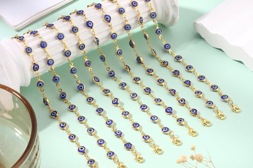 Evil eye bracelets with blue glass charms draped in rows on a mint green background, showing 14K gold plated gold-tone chains in detail.