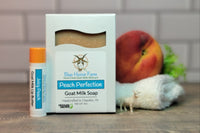 Goat milk soap and lip butter in Peach Perfection scent with a real ripe peach sitting on a white wash cloth.