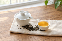 Gaba Oolong from Nepal brewed in a white gaiwan, with a cup of golden tea and rolled oolong leaves on linen on a wooden table