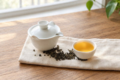 Gaba Oolong from Nepal brewed in a white gaiwan, with a cup of golden tea and rolled oolong leaves on linen on a wooden table