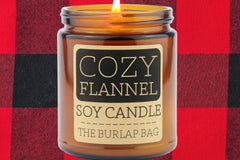 Cozy Flannel 9oz soy candle by The Burlap Bag, peppercorn and musk scented amber jar on a red and black buffalo plaid