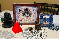 call of the morrigan Oracle deck with a mountain style backflow incense burner, a red pyramid candle, jewelry, crystals and incense