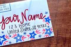 Hand-decorated patriotic envelope with red and blue stars, handwritten sample name, home address and U.S. mailing details.