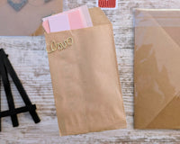 Paper pouch full of pink paper strips poking out the top. A gold metallic paperclip bent to spell the word love is attached on one side.