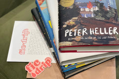 Items laid out on a green velvet chair, including books, a sticker, a brown paper packing envelope, and a FicDrip flyer.