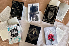 A table with 6 books laying on it. Three books have a dark cover with gold lettering. the other three have a bright cover. 