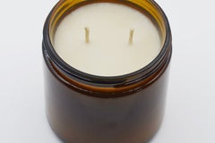 Top view of an unlit 16oz Burlap Bag soy candle showing two cotton wicks set in smooth cream soy wax inside the amber jar