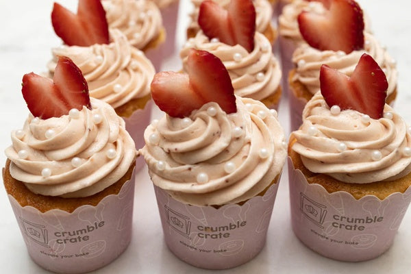 Bright lemon cupcakes topped with pink strawberry buttercream swirls and white sugar pearls in a baking kit setup