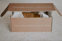 A custom Village Thrive terracotta box with white text opening to reveal tissue paper and the gift items inside.