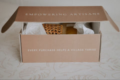 A custom Village Thrive terracotta box with white text opening to reveal tissue paper and the gift items inside.
