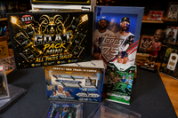 The G.O.A.T Pack Mini sealed multi-sport trading card mystery box displayed with basketball, baseball and football card packs, hobby boxes a