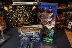 The G.O.A.T Pack Mini sealed multi-sport trading card mystery box displayed with basketball, baseball and football card packs, hobby boxes a