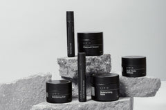 High quality photo of 6 mens self care and skin care products in black color. With the products standing on rocks