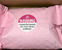 Open shipping box with pink protective bubble wrap packaging inside, featuring a warning label sticker and presentation of how the product i