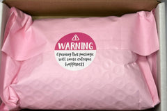 Open shipping box with pink protective bubble wrap packaging inside, featuring a warning label sticker and presentation of how the product i
