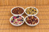 Four caffeine-free teas from The Tea Smith in white dishes: cinnamon rooibos, chamomile with lemon, a butterfly pea blend and ginger orange