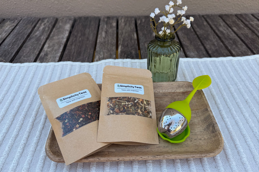Displayed on a table with placemat, a Mini Monthly Subscription pack, two packs of loose leaf teas, with first month silicone leaf infuser 