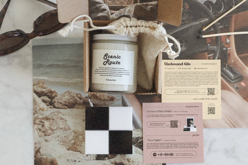A Vellabox subscription box featuring The Glow Box candle with a croissant scent, surrounded by breakfast items and fresh fruit