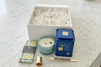 Contents of our Blue Hue gift box featuring Canadian Honey Earl Grey Tea tin, Tahiti soy wax candle, Sicilian lemon dark chocolate bar