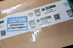 A Cardboard box with custom printed tape with "Lil Monsters Bird Toys", a logo, QR code, website, and "Caution: Contents May Attract Parrots