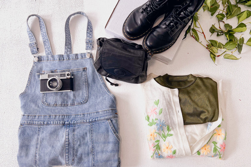 Overalls and a camera on top of them, flat lay vintage cardigan with silk olive green top and black accessories to match. 