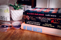 Brown box filled with a diverse collection of books in multiple genres, including crime thrillers, romance, and fantasy