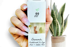 Close up of a Chamomile, Sandalwood, Sage Cuticle Oil Trio by Greenmade goods against a light background with a plant.