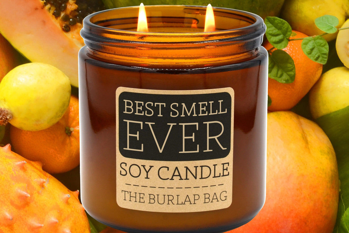 Lit Best Smell Ever 16oz double-wick soy candle by The Burlap Bag, amber jar set against papaya, guava, and citrus fruit