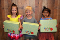 three children are standing in front of a wooden wall. they are each holding a wiggle worms kit box..